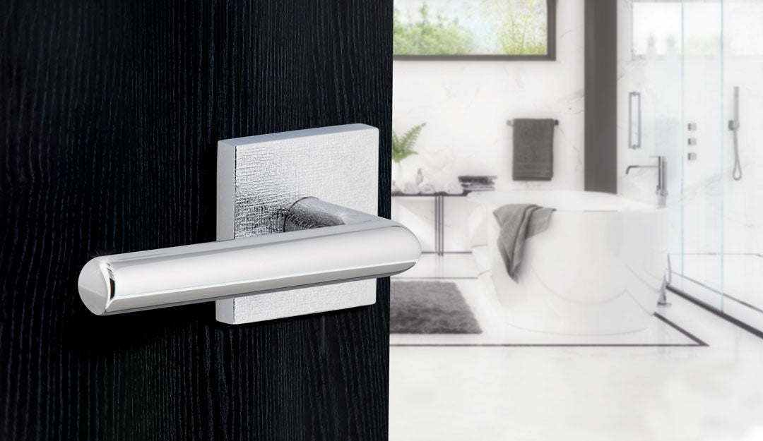 a black door with bright chrome contemporary hardware with a lever from viaggio hardware opening into a modern white luxury bathroom